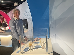 Mann in grauem Pullover und in Jeans an einer Glasvitrine, die Exponate enthält