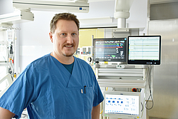 Porträtaufnahme von Dr. Christoph Busjahn in einem Intensivzimmer. Im Hintergrund sind Bildschirme zu sehen