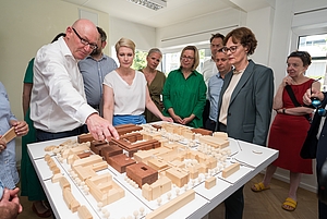 Gruppe von Menschen steht um einen Tisch mit einem Architekturmodell aus Holz und Pappe in einem hellen Raum