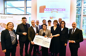 Eine Gruppe Menschen hält einen stilisierten großen Scheck, auf dem "Fördermittelbescheid" steht