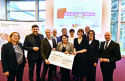 Eine Gruppe Menschen hält einen stilisierten großen Scheck, auf dem "Fördermittelbescheid" steht