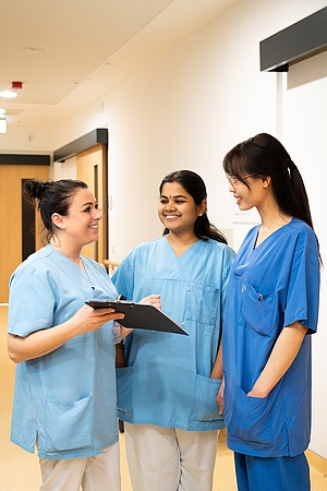 Eine deutsche, eine indische und eine vietnamesische Krankenschwester unterhalten sich auf einem Stationsflur