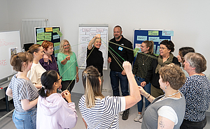 Menschen im Kreis halten Fäden an der Hand, die in der Mitte zusammen führen. 