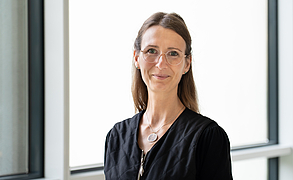 Frau mit dunkelblonden, nach hinten gekämmten Haaren, Brille, dunkler Kleidung